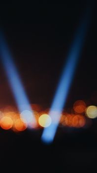 Blurry bokeh city lights at night with blue spotlights creating an abstract effect.
