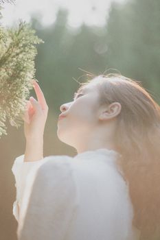 A peaceful moment of a woman touching leaves in soft sunlight, evoking tranquility.