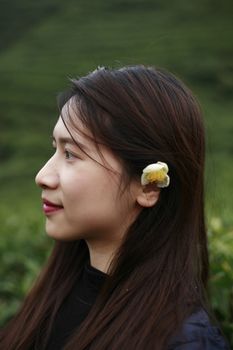 Side profile portrait of a woman with long hair and a flower, serene outdoor setting.