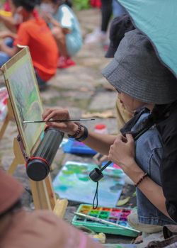 A young Vietnamese woman painting on a canvas in a lively outdoor setting in Ho Chi Minh City.