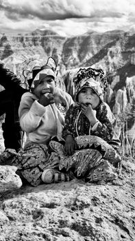 Two children in traditional attire sitting outdoors on rocky terrain in Mexico. Black and white photo.