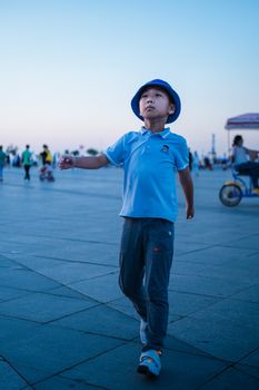A young boy walks confidently in an urban city square during a calm summer evening.