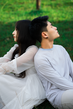 A young couple in white outfits sitting back to back on grass in Dalat, Vietnam on a sunny day.