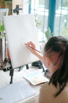 Girl sketching on canvas indoors, natural lighting and creative ambiance.