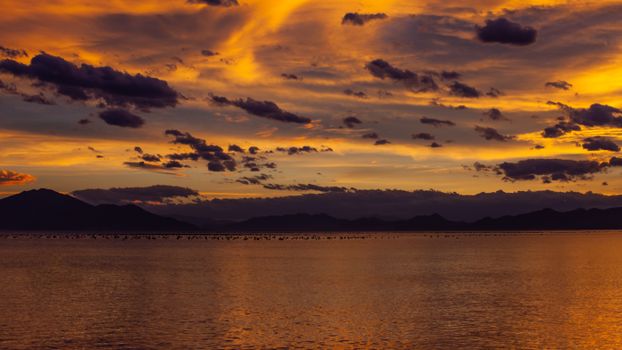 Vibrant sunset over tranquil waters in Bombinhas, Brazil, with dramatic sky and mountains.
