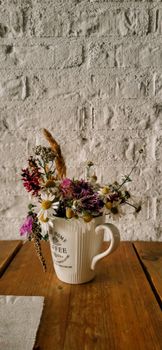 Charming arrangement of wildflowers in a coffee mug against a rustic wall.