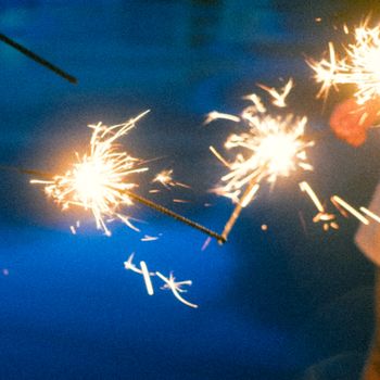 Group of people holding sparklers against a vibrant night sky.
