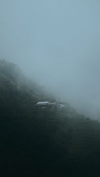 A misty landscape featuring a solitary house nestled on a foggy hillside in Panauti, Nepal.