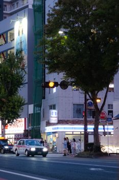 Street view of downtown Fukuoka, Japan at twilight with pedestrians and traffic, capturing the city life.