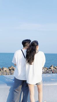 A young couple gazing at the ocean, standing on a sunny seaside promenade.