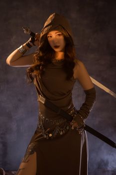 Dark and dramatic portrait of a mysterious warrior woman with a sword and hooded attire.