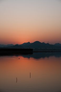 A peaceful sunset casting warm hues over a lake with mountains in the background, creating a serene reflection.