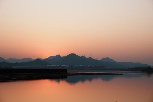 Beautiful sunset view over a calm lake with mountains silhouetted in the background, reflecting serene colors.