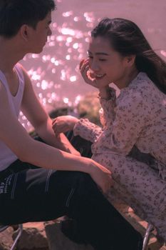 Young couple sitting together by the water, sharing smiles and affection in natural sunlight.