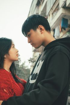 A young couple looking at each other warmly outdoors with a city backdrop.