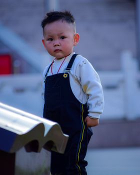 Cute child in overalls standing outdoors in China, showcasing a thoughtful expression.
