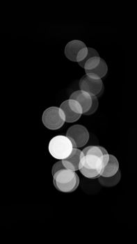 A vertical black and white abstract image featuring a circular bokeh pattern on a dark background.