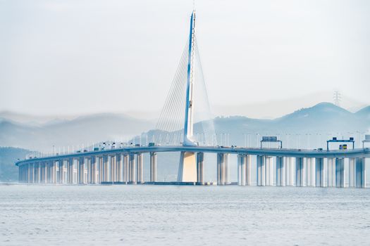 A magnificent cable-stayed bridge extending over calm waters with scenic mountains in the background.