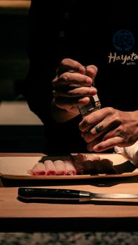 Chef sprinkling seasoning on sushi rolls in a dimly lit kitchen setting at Hayata Hotel, Taiwan.