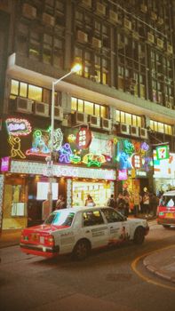 Bustling night street in Hong Kong with vibrant neon signs and iconic taxi. Urban nightlife at its best.