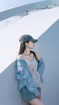 Young woman in trendy outfit leaning on urban architecture during a bright day.