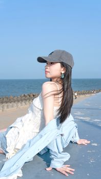 A young woman in casual summer attire sitting by the seaside, enjoying the sunny day.