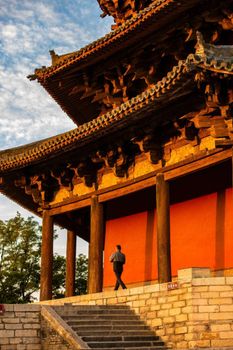 A man walks by an ancient wooden pagoda bathed in sunset light in Shaanxi, China.