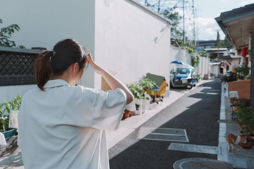 A woman walks through a sunlit alley in an urban area, shielding her eyes.