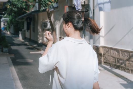 Young woman in a white blouse walking down a sunlit alley, capturing the essence of a summer day.