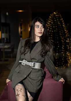 Stylish woman in blazer posing indoors with festive lights creating a warm atmosphere.