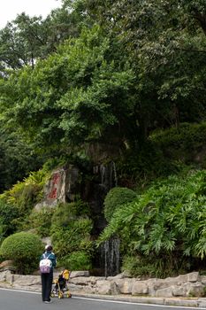 A scenic waterfall surrounded by lush greenery with a person and stroller in Guangzhou.