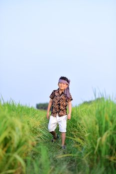 A joyful young boy walks through a vibrant green field, enjoying a sunny day outdoors.