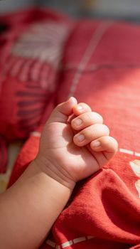 Tender moment captured as a baby's hand rests on a red blanket, sunlight casting warm highlights.