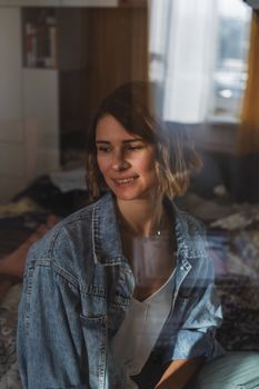 A cheerful woman in denim is smiling indoors, reflecting soft daylight.