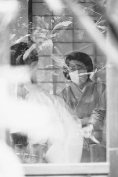 Masked individuals reflected through glass in a serene setting.