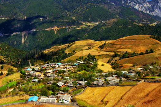 Aerial view of colorful rural village surrounded by lush mountains in Lijiang, Yunnan, China.