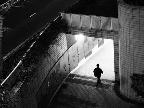 Moody black and white photograph of a lone figure in a Hong Kong city tunnel.