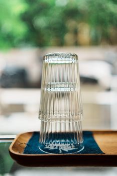 Artistic shot of two stacked clear glasses on a blue napkin with blurred greenery outside.