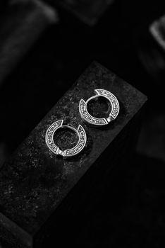 Close-up of intricate silver hoop earrings on a dark stone surface.