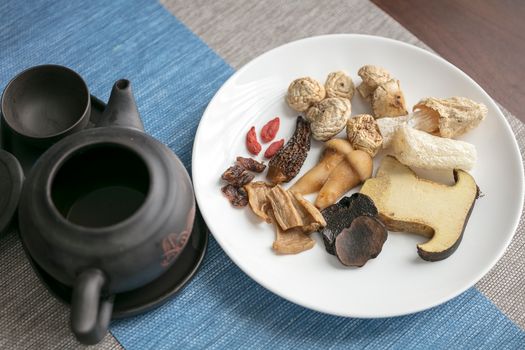 A plate of assorted dried Chinese herbs and mushrooms with a traditional teapot.