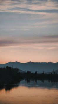 Tranquil sunset over a lake with mountain silhouettes and a peaceful sky reflection.